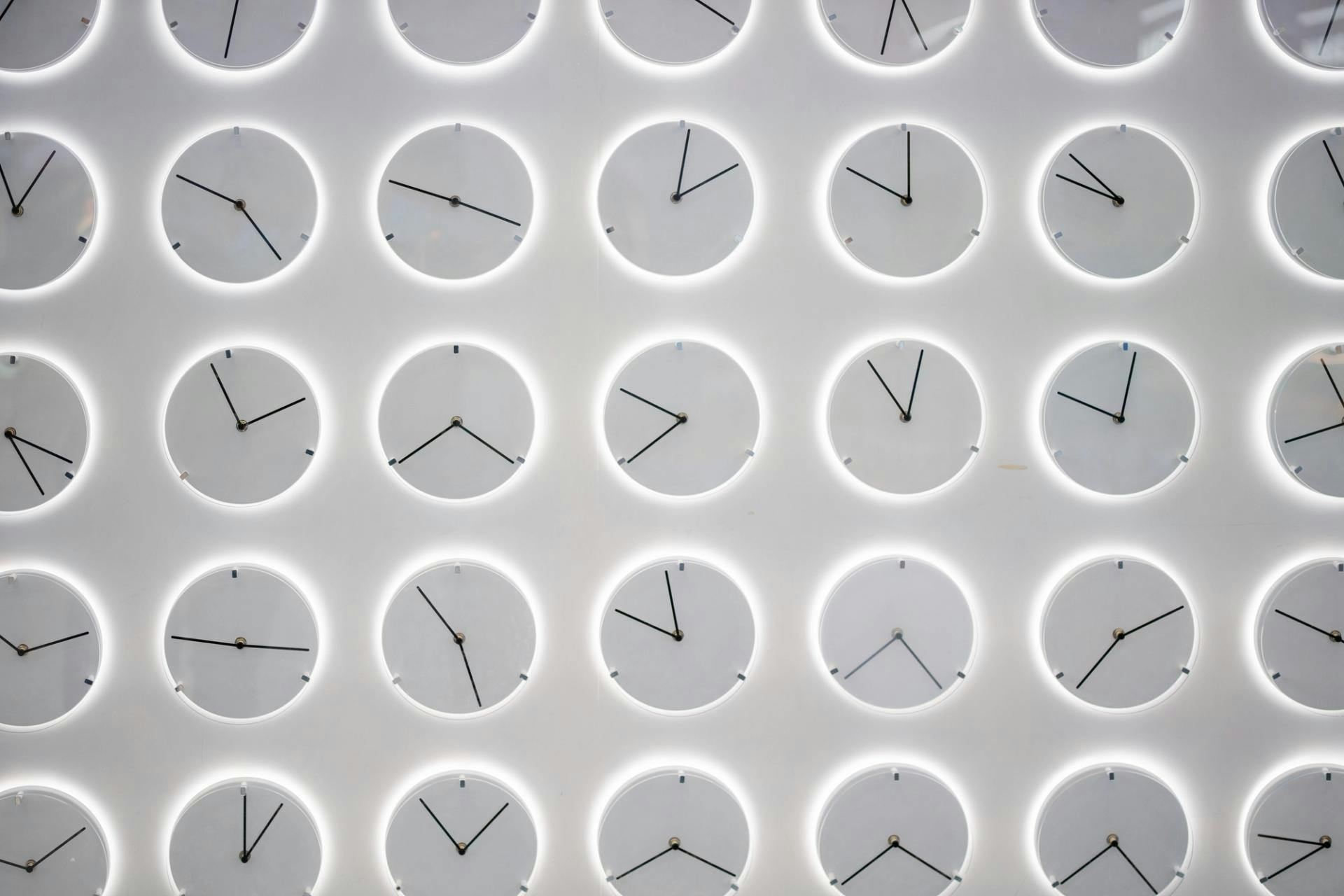 Clocks showing difference times with a white background in structured rows and columns with a white glow around each clock.